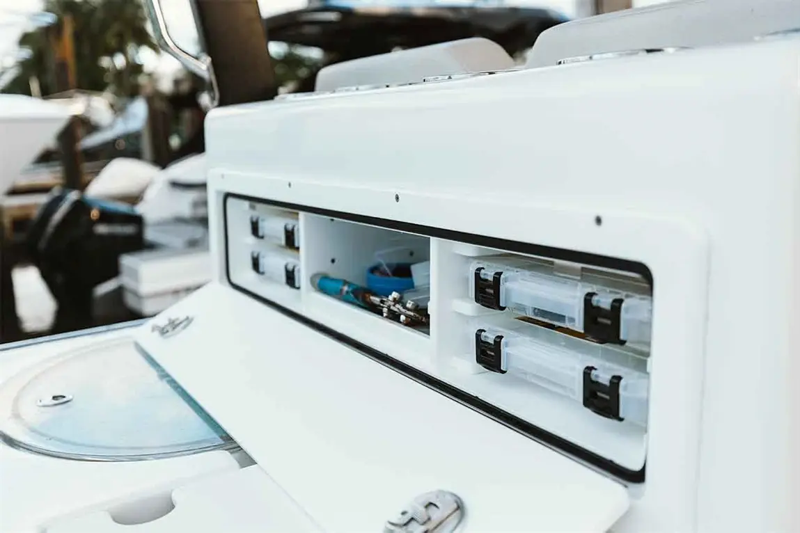 Close-up of a white boat control panel with storage compartments, featuring tools and fishing equipment organized inside.
